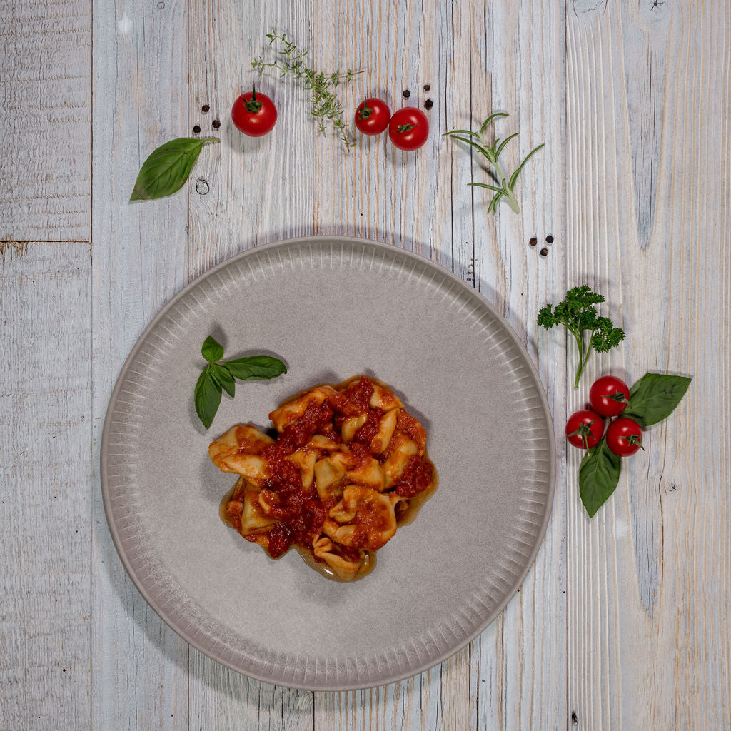 Tortelloni mit Tomatensauce angerichtet auf einem Teller garniert mit Tomaten