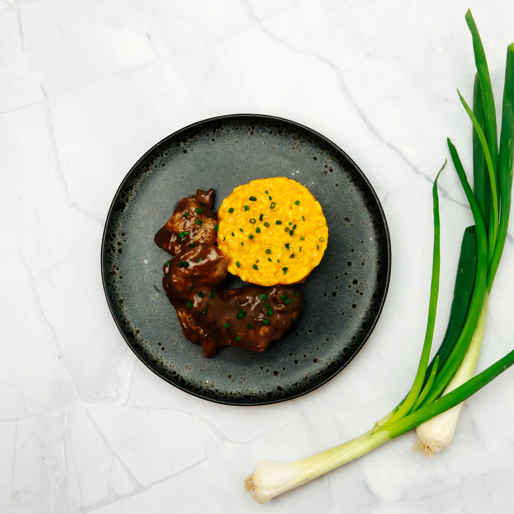 Coq au vin als Serviervorschlag mit Safran risotto auf einem Dunklen Teller angerichtet